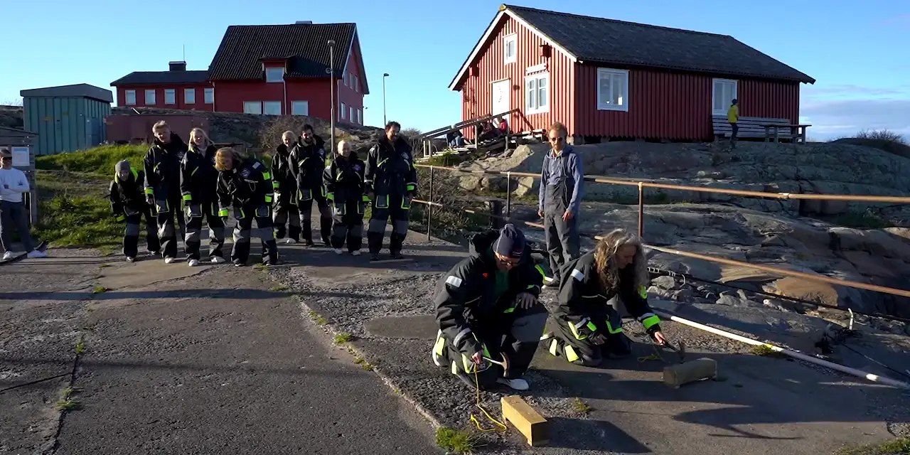 Ett företagsgäng i overaller jublar framför röda sjöbodar i skärgården